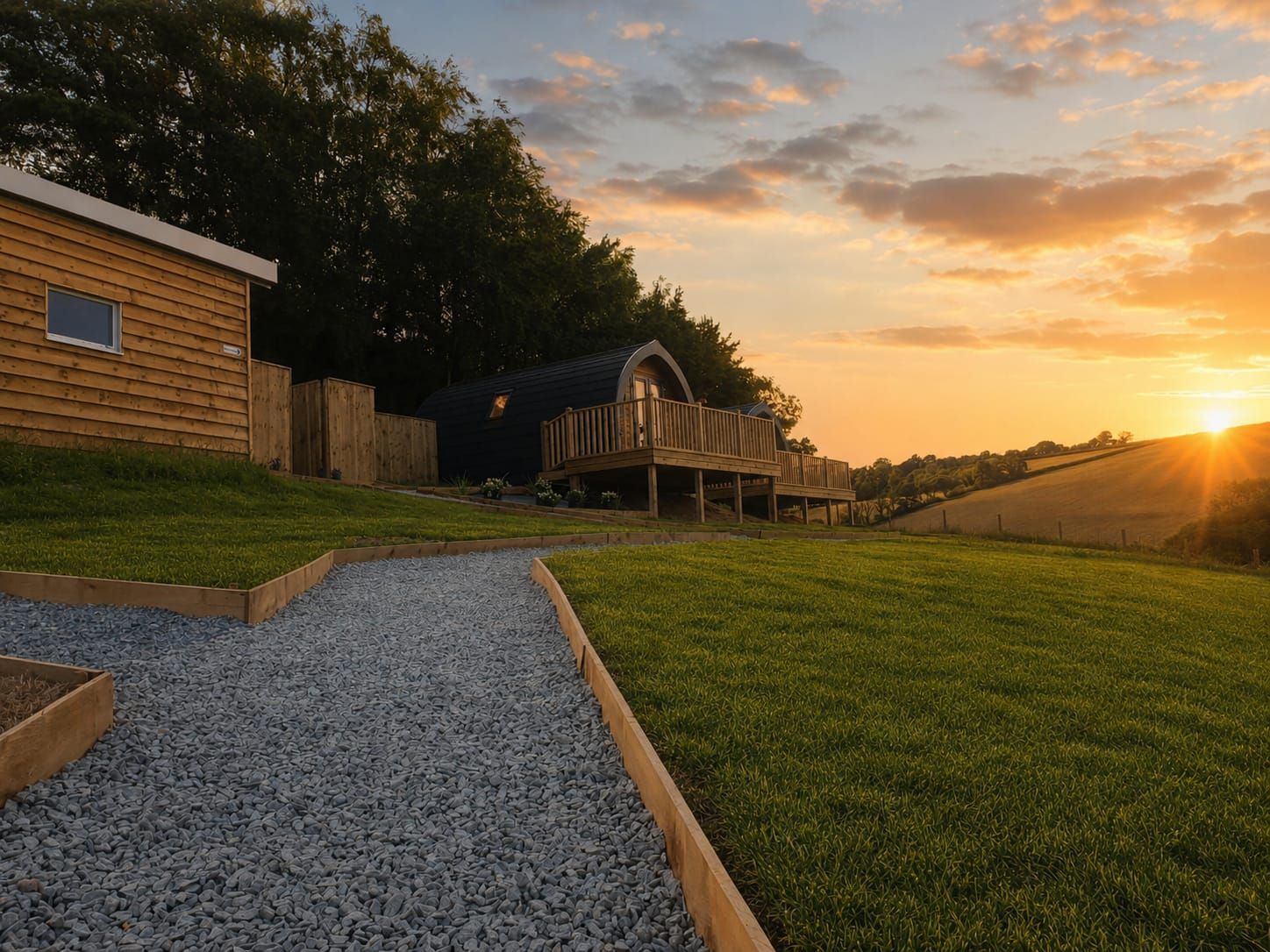 Gravel path beside a cabin and bench overlooking a grassy field at sunset