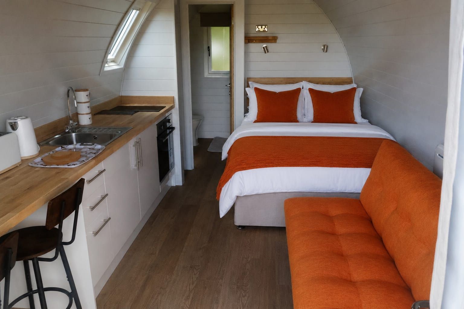 Compact tiny home interior with kitchenette, bed, and orange sofa
