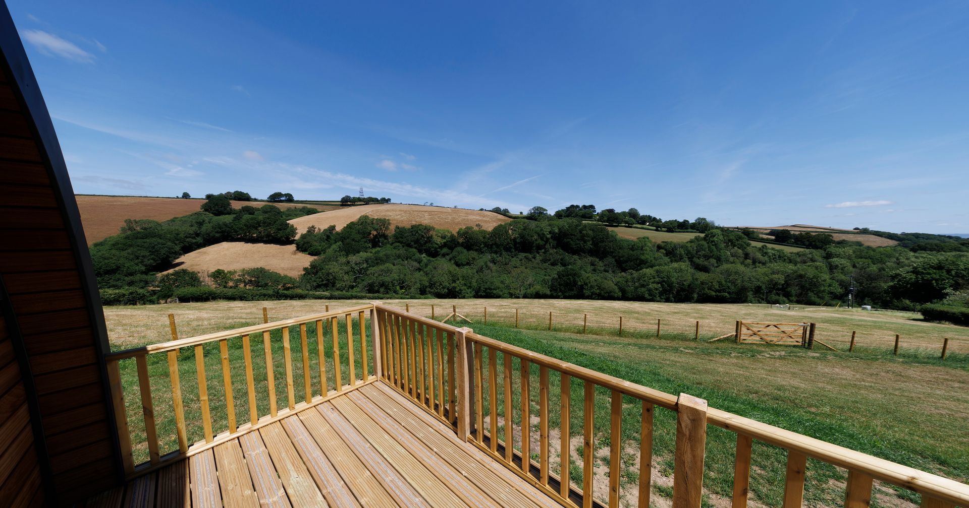 Wooden deck overlooking grassy fields and rolling hills under a clear blue sky