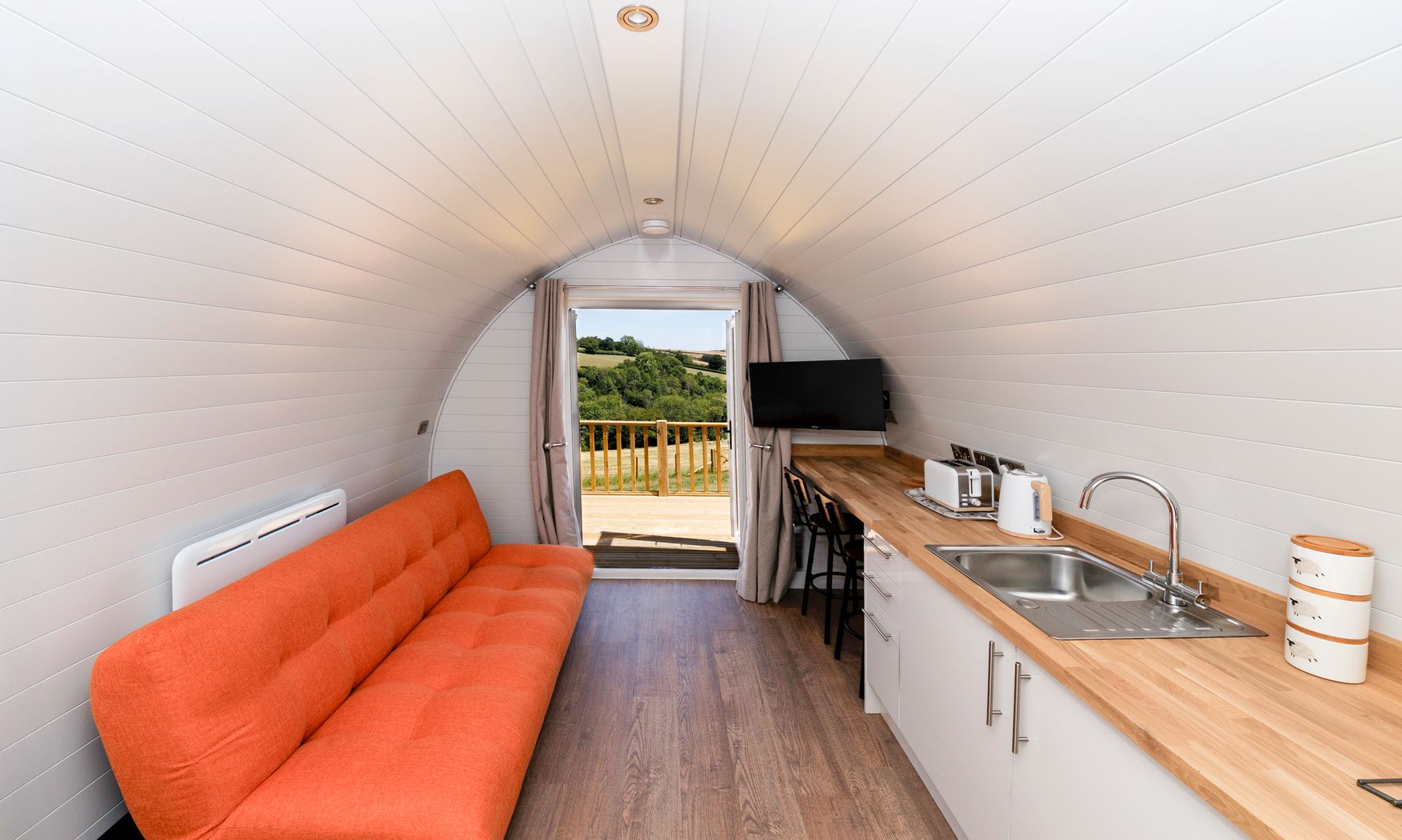 Cozy tiny house interior with orange sofa, kitchenette, and open door to a grassy yard