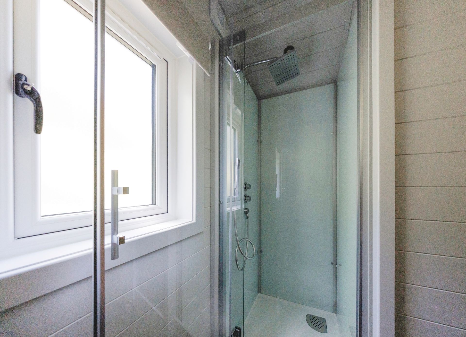 Modern bathroom with a glass shower enclosure beside a bright window.