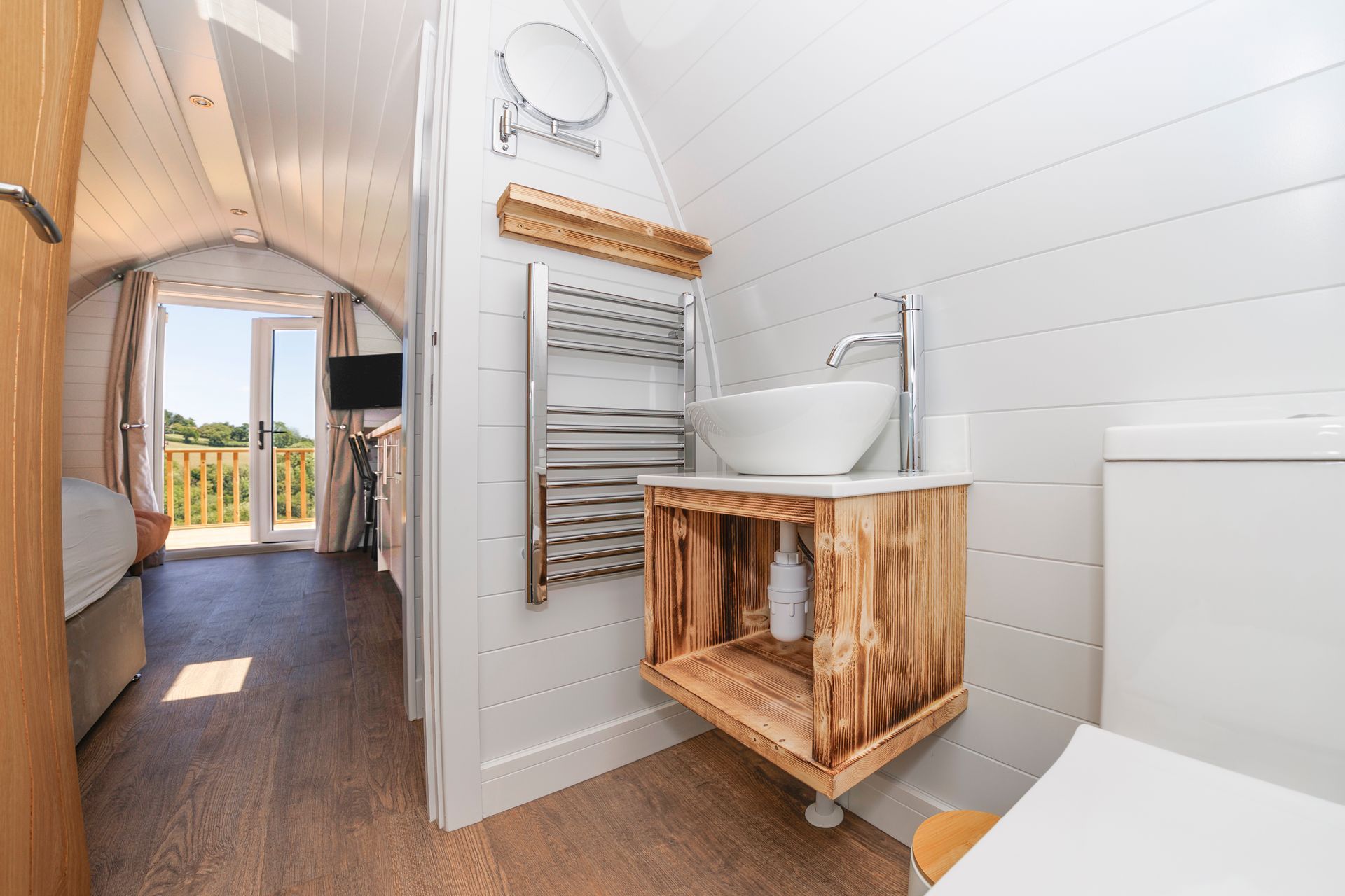 Bright narrow hallway with wood floors, white paneled walls, and a rustic sink vanity beneath a towel rack.