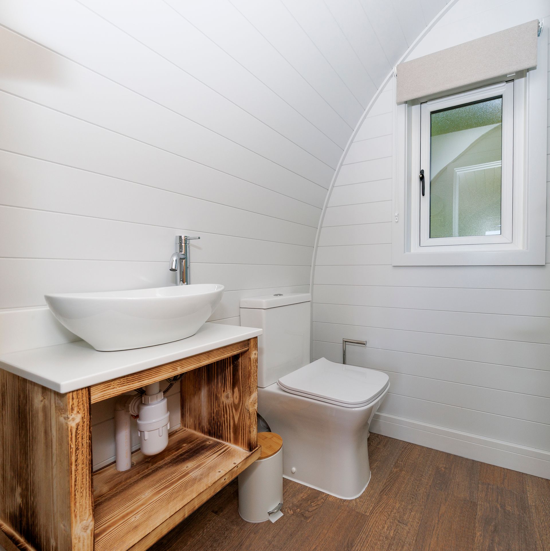 Modern bathroom with curved white walls, wooden vanity, sink, toilet, and small window