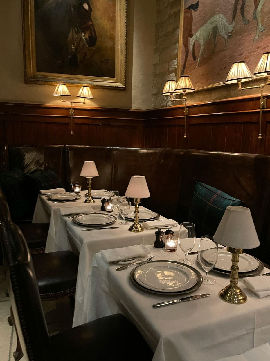 Elegant restaurant table set with white linens, lamps, and candlelight in a wood-paneled dining room