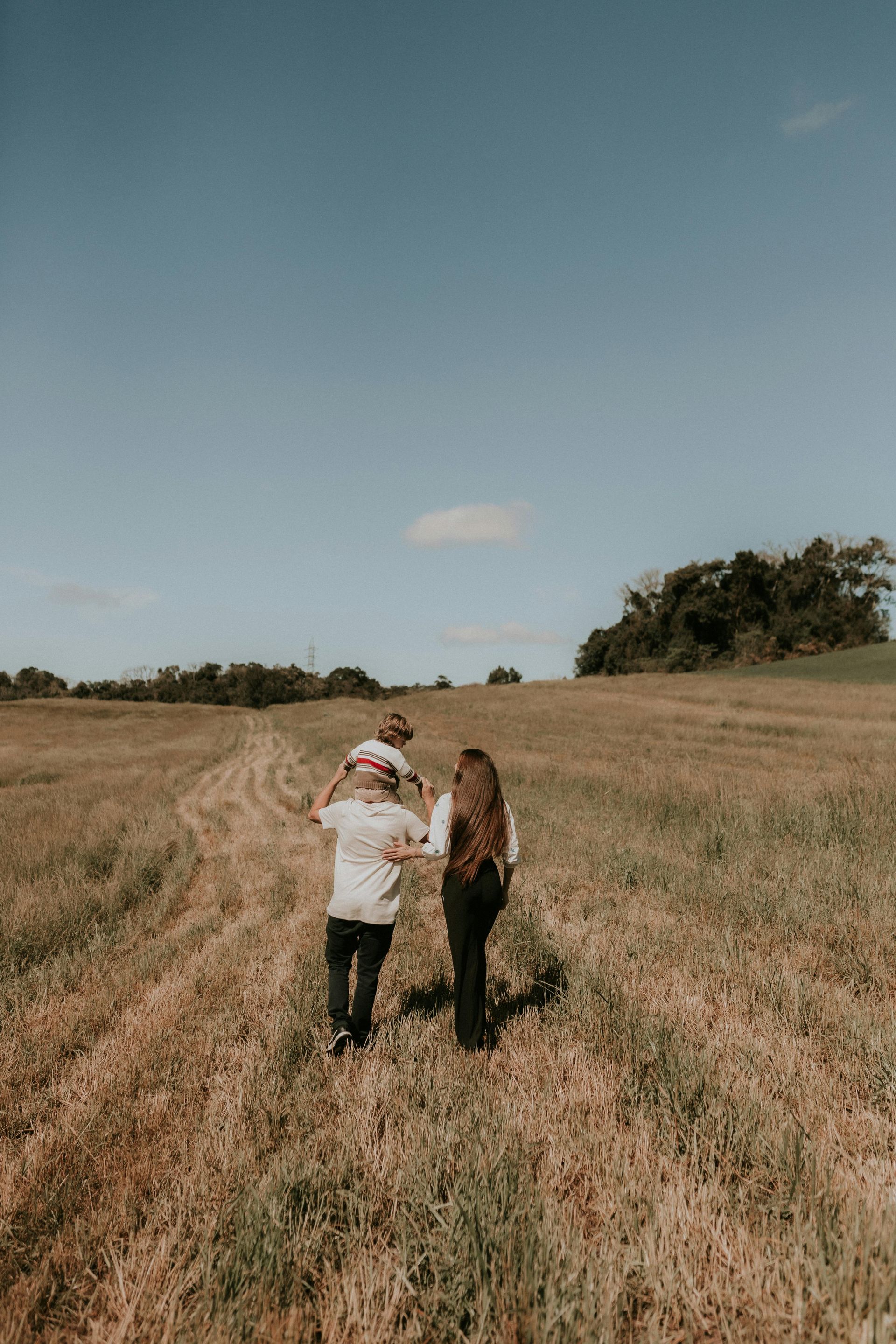 Two people walking through a dry grassy field under a clear blue sky
