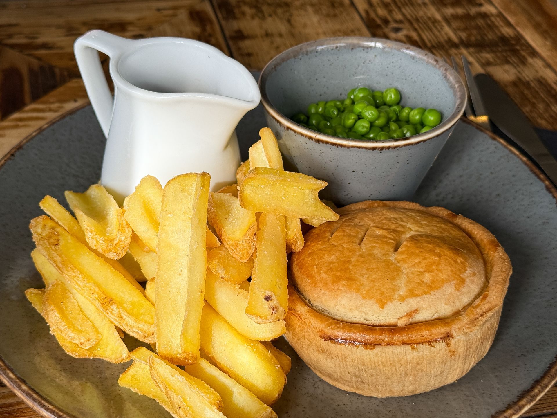 Fries, a meat pie, peas, and gravy on a gray plate