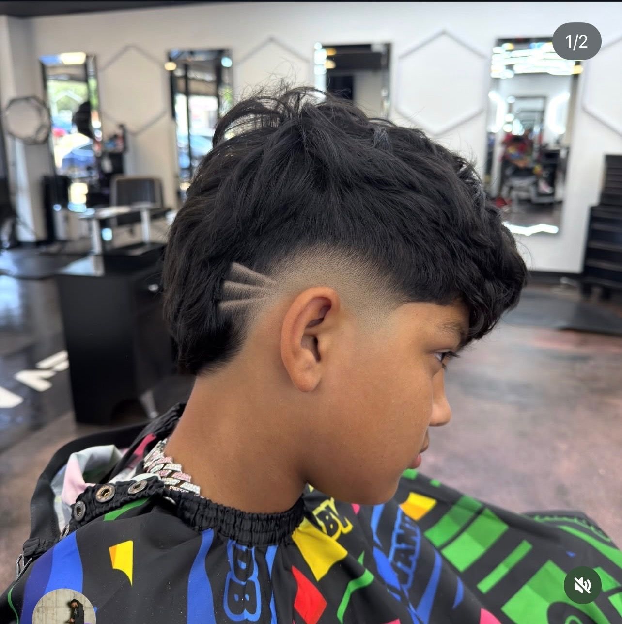 Side profile of a person with a textured fade haircut in a barbershop, wearing a colorful cape