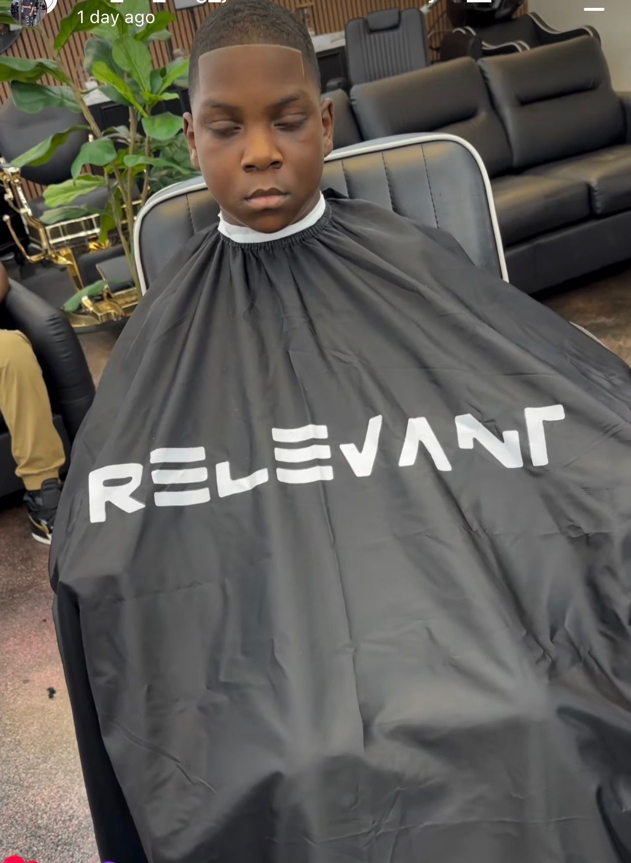 Person in a black RELEVANT haircut cape sitting in a salon chair with a face mask under the chin