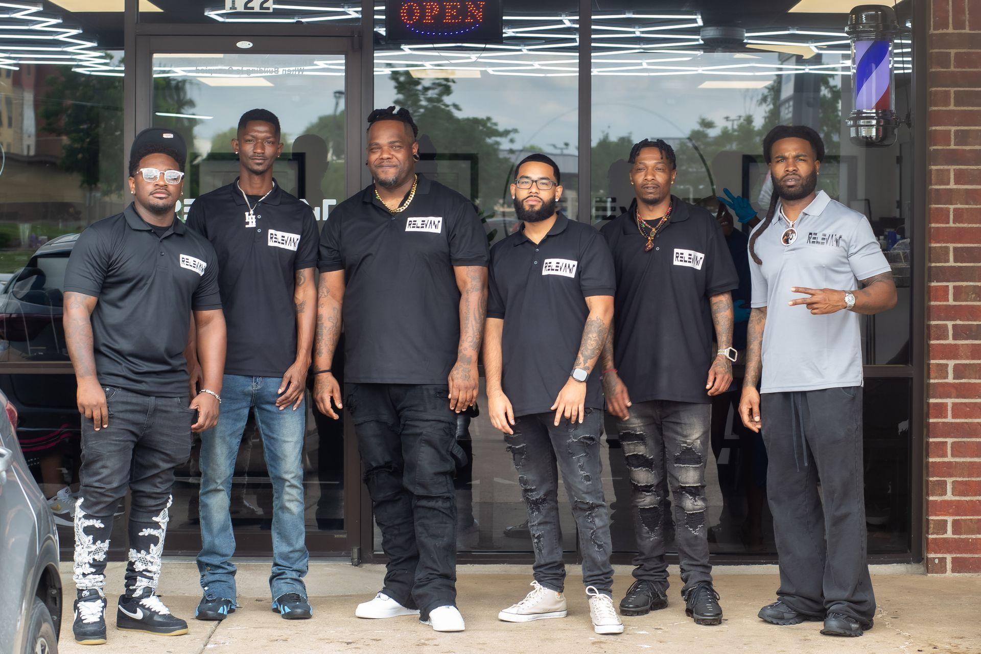 Six mechanics standing outside an auto shop, wearing black and gray work shirts.