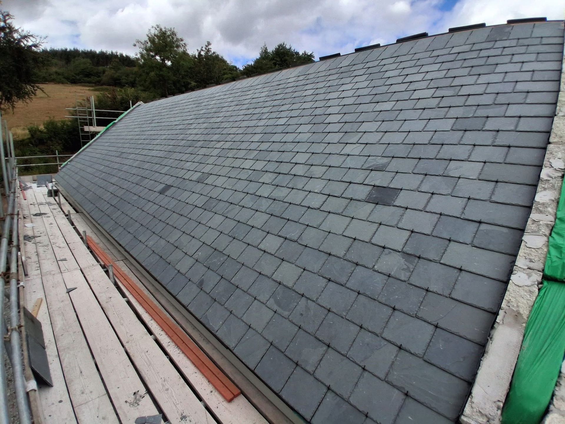 Finished grey slate roof beside scaffolding