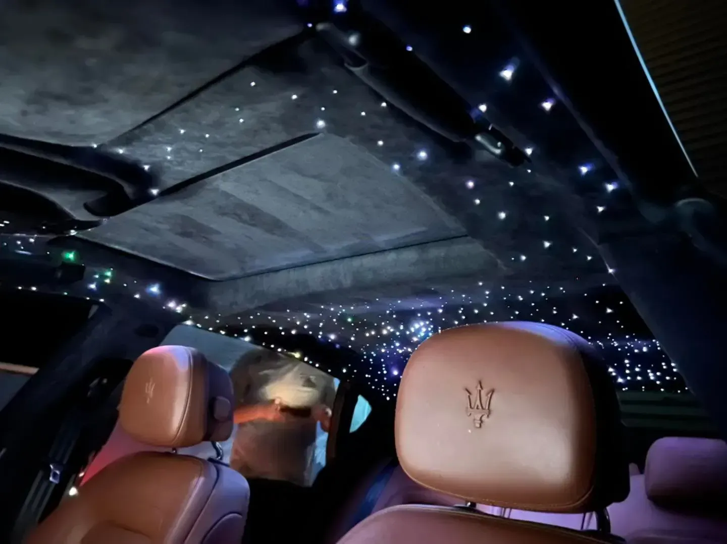 Interior of a car with star-like lights in the ceiling, brown leather seats, and a Maserati logo.