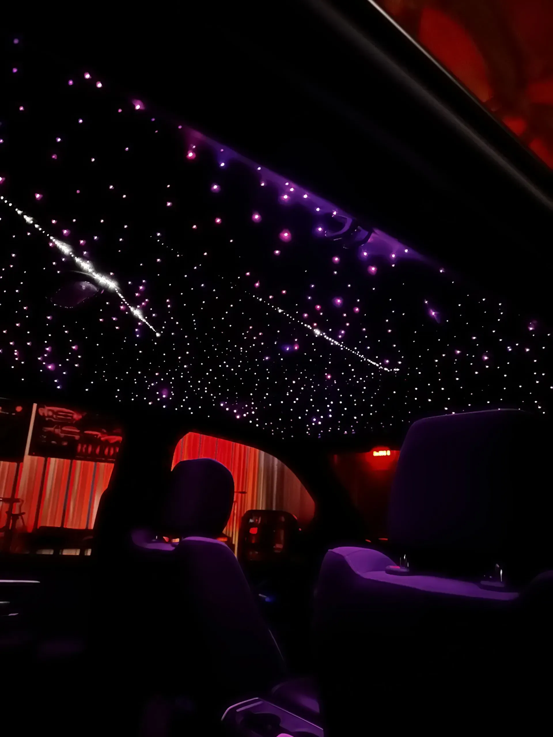 Car interior with a starry night ceiling illuminated in purple.