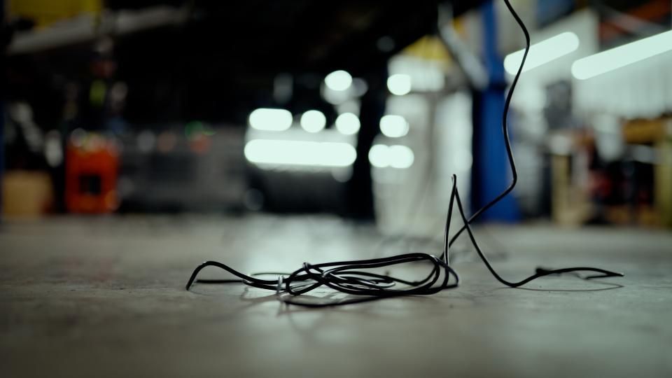 Loose black cable on a garage floor, with blurred headlights and workshop lights in the background
