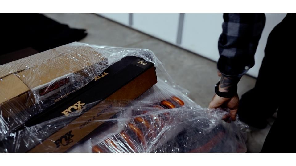 Plastic-wrapped coffin being carried indoors by a person in black clothing