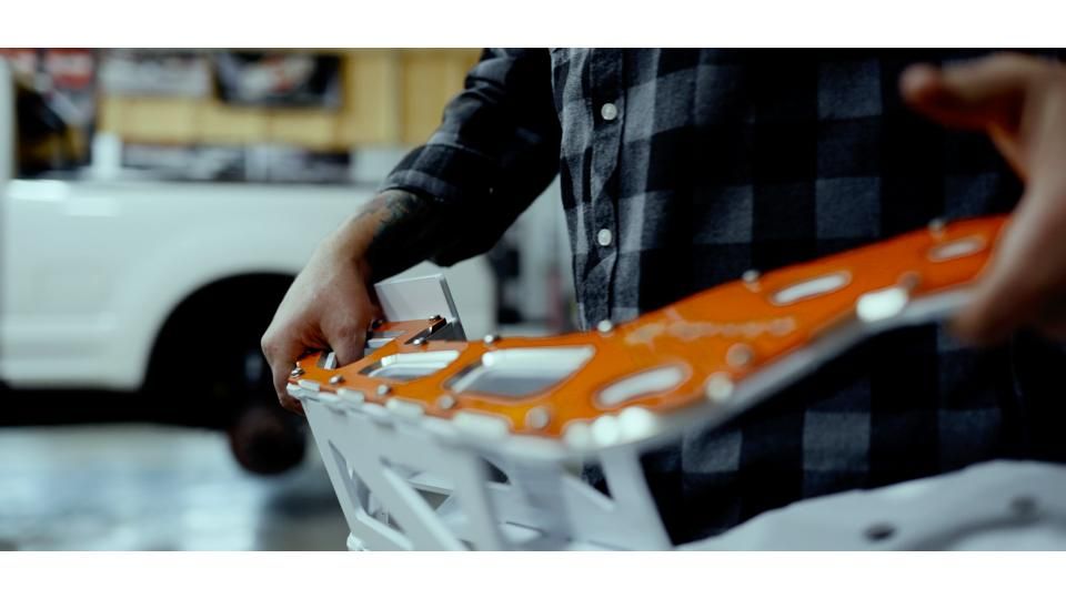 Person holding an orange-and-white model car in a workshop or garage
