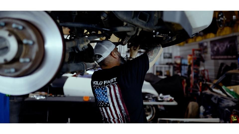 Mechanic working under a vehicle in a garage, with a wheel and underside visible