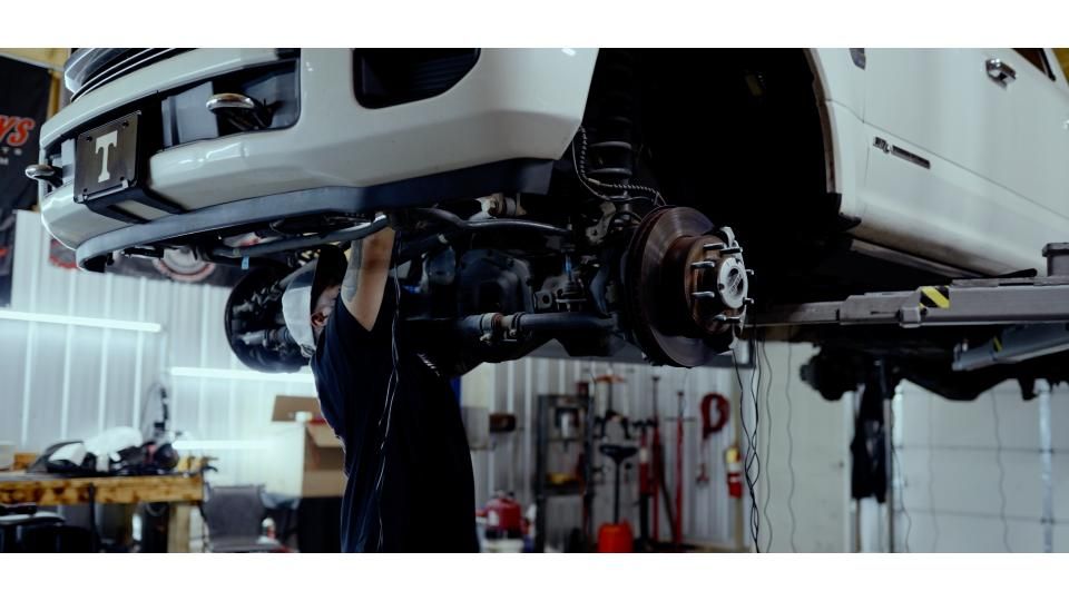 Mechanic working under a lifted white vehicle in an auto repair shop