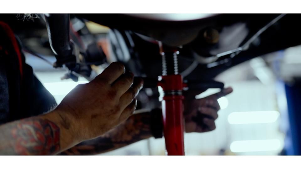 Hands working under a vehicle on a red jack stand in a garage