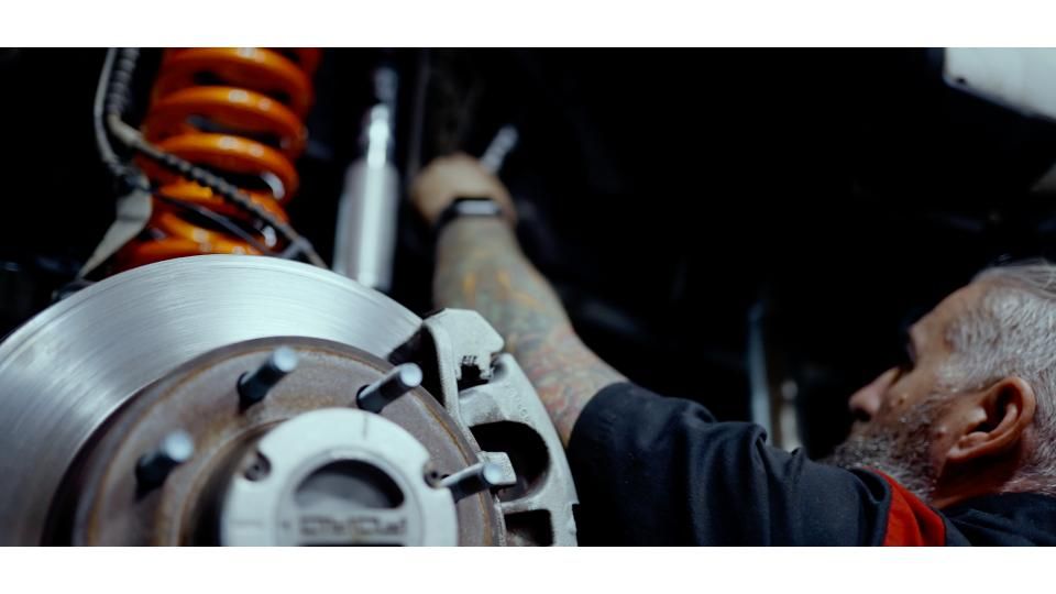 Mechanic working on a car’s brake assembly beside a bright orange suspension spring