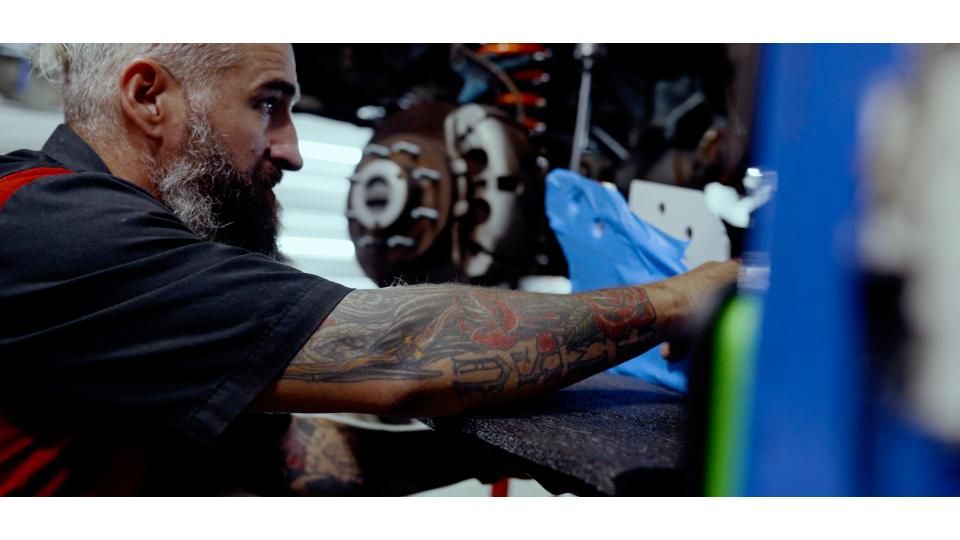 Mechanic using a blue glove to work on a car brake assembly in a workshop