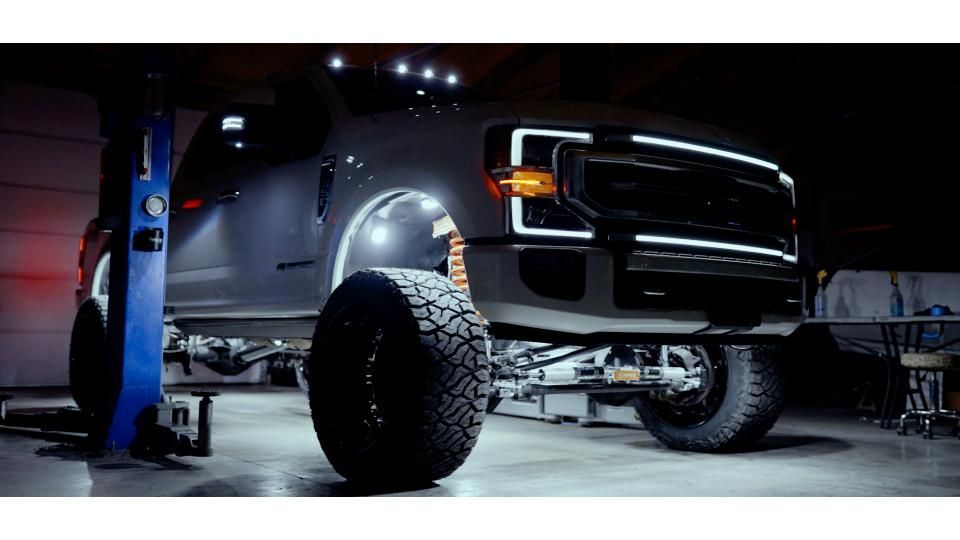 Lifted black pickup truck on a lift in a garage, with oversized off-road tires and chrome front grille.