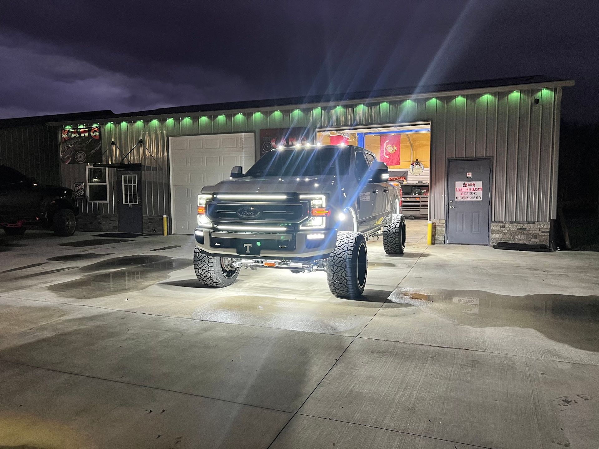 Black Ford F-150 truck with chrome rims on a lift inside a garage with an American flag on the wall.