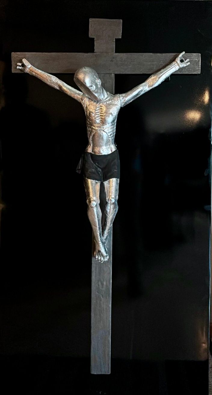 Crucifijo de plata con la figura de Jesús en una cruz oscura sobre fondo negro.