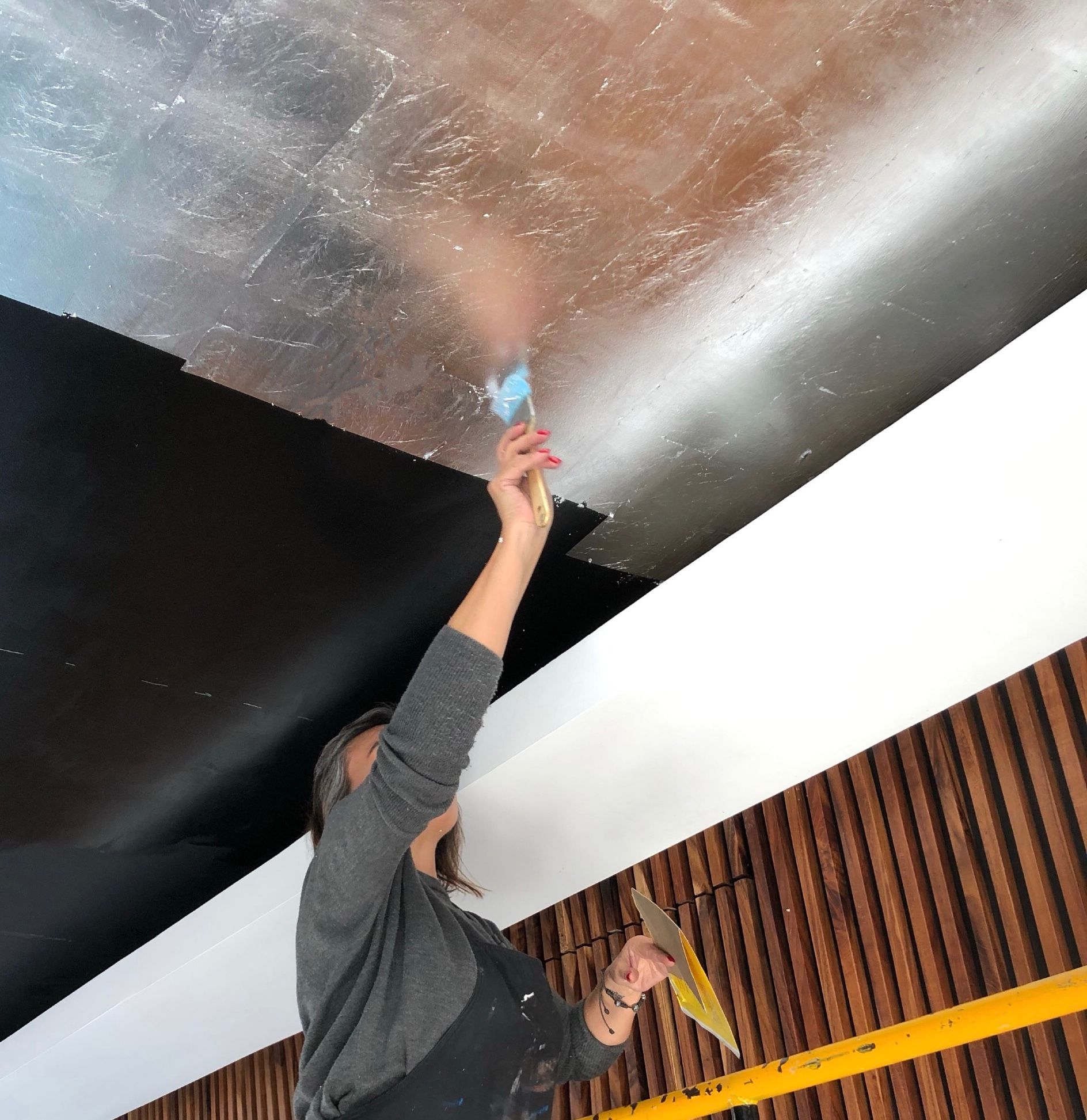 Una persona subida a una escalera pinta con aerosol el techo de una habitación con pintura azul.