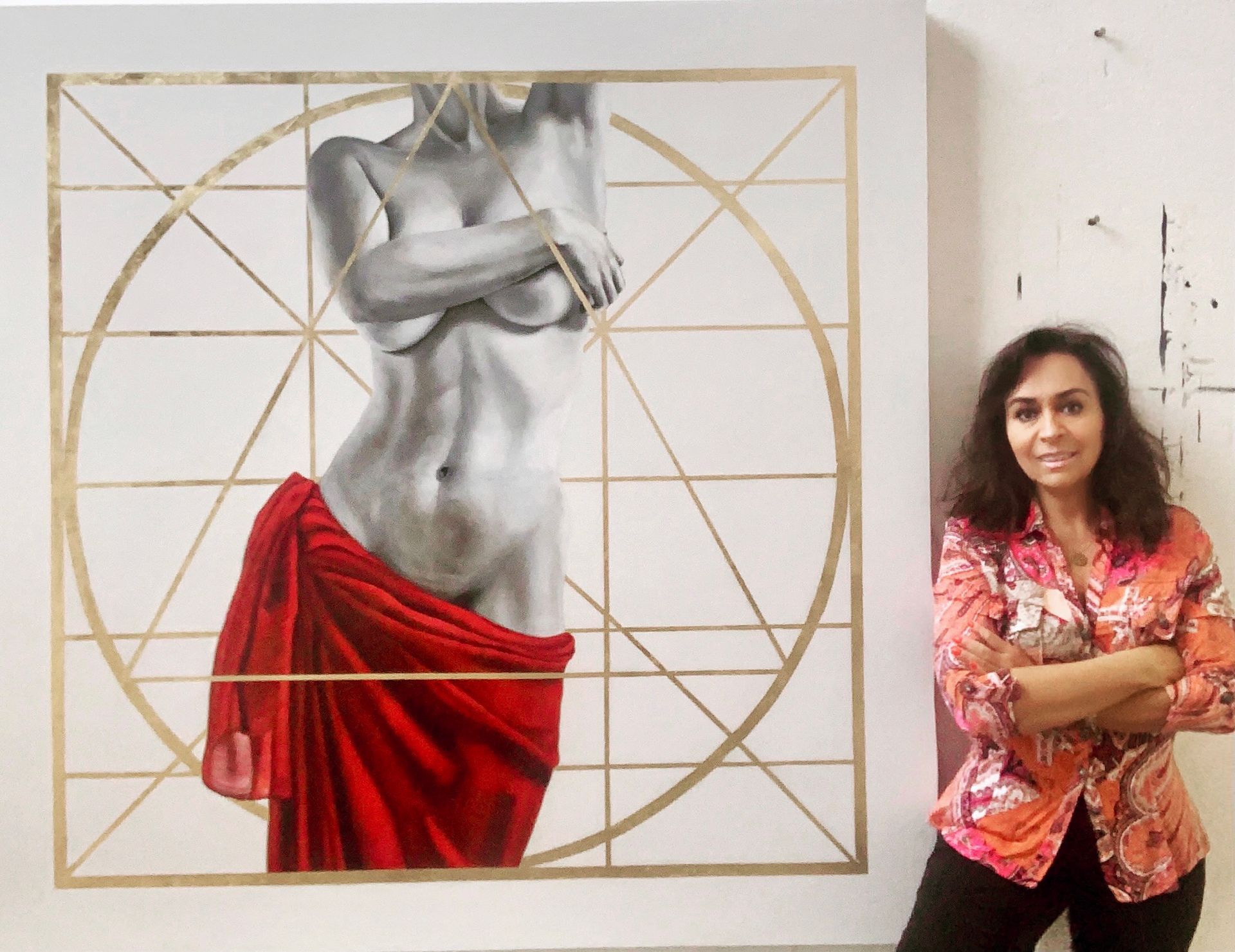 Mujer junto a un torso pintado en escala de grises con líneas geométricas doradas y un drapeado rojo.