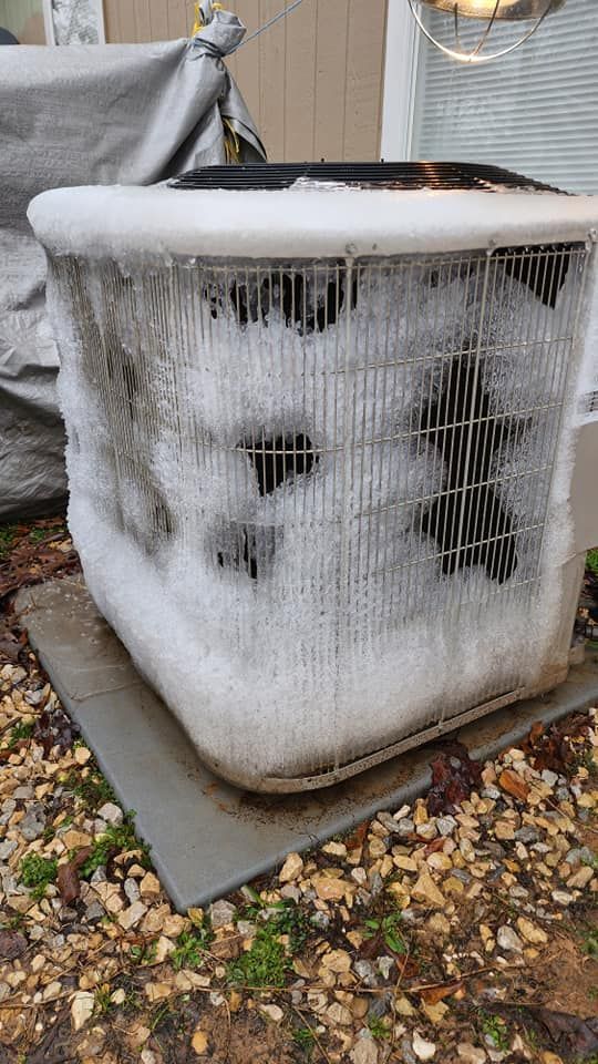 An air conditioner is covered in ice and is sitting on the ground.