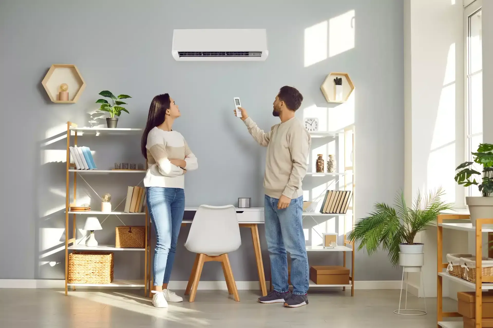 A man and a woman are standing in a living room looking at a wall mounted air conditioner.