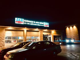 A & R Auto Repair shop at night, illuminated sign above garage doors. Cars parked outside. | A & R Auto Repair