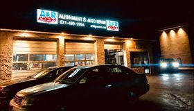 A & R Auto Repair shop at night, illuminated sign above garage doors. Cars parked outside. | A & R Auto Repair