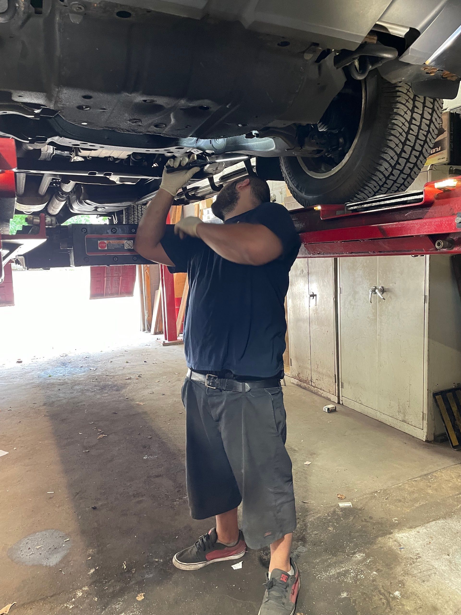 Mechanic working under a car raised on a lift. He wears a mask and holds a tool. Garage setting. | A & R Auto Repair