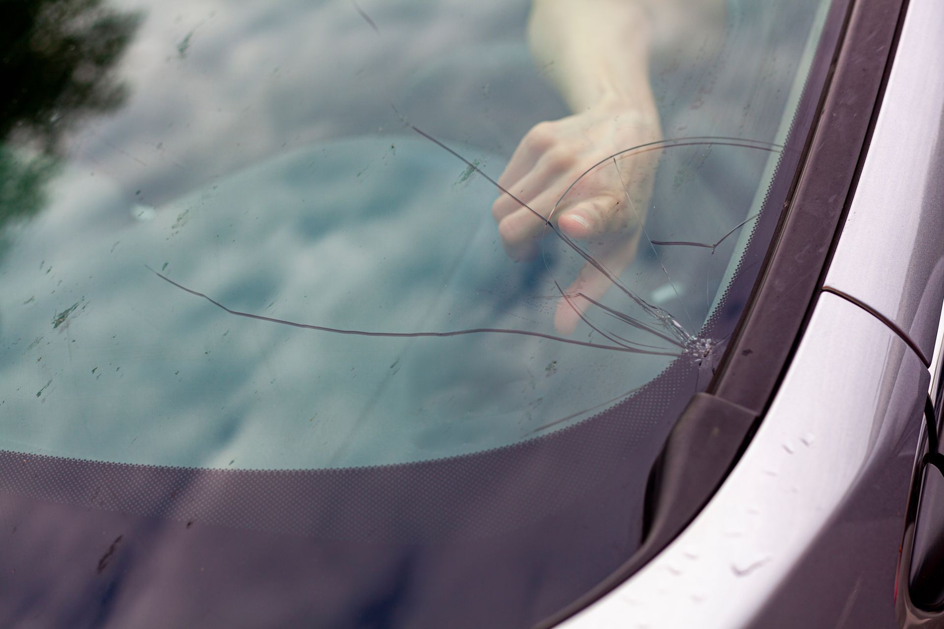 Pare-brise de voiture fissuré avec une main à l'intérieur, près de l'essuie-glace et de la carrosserie.