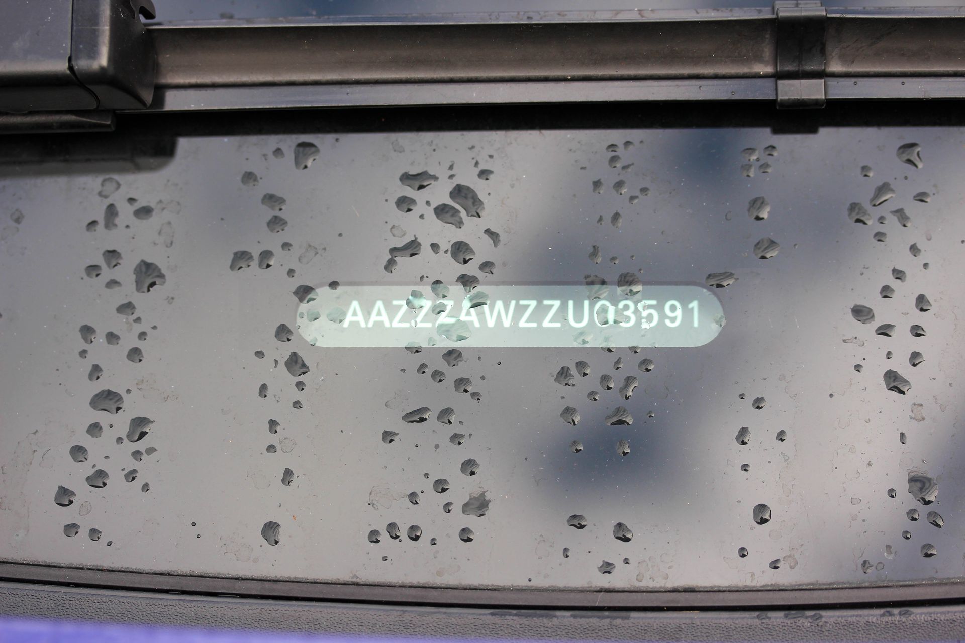 Gros plan sur le numéro VIN d'un véhicule (AA22Z4WZZU03591) sur le pare-brise, masqué par des gouttelettes d'eau.