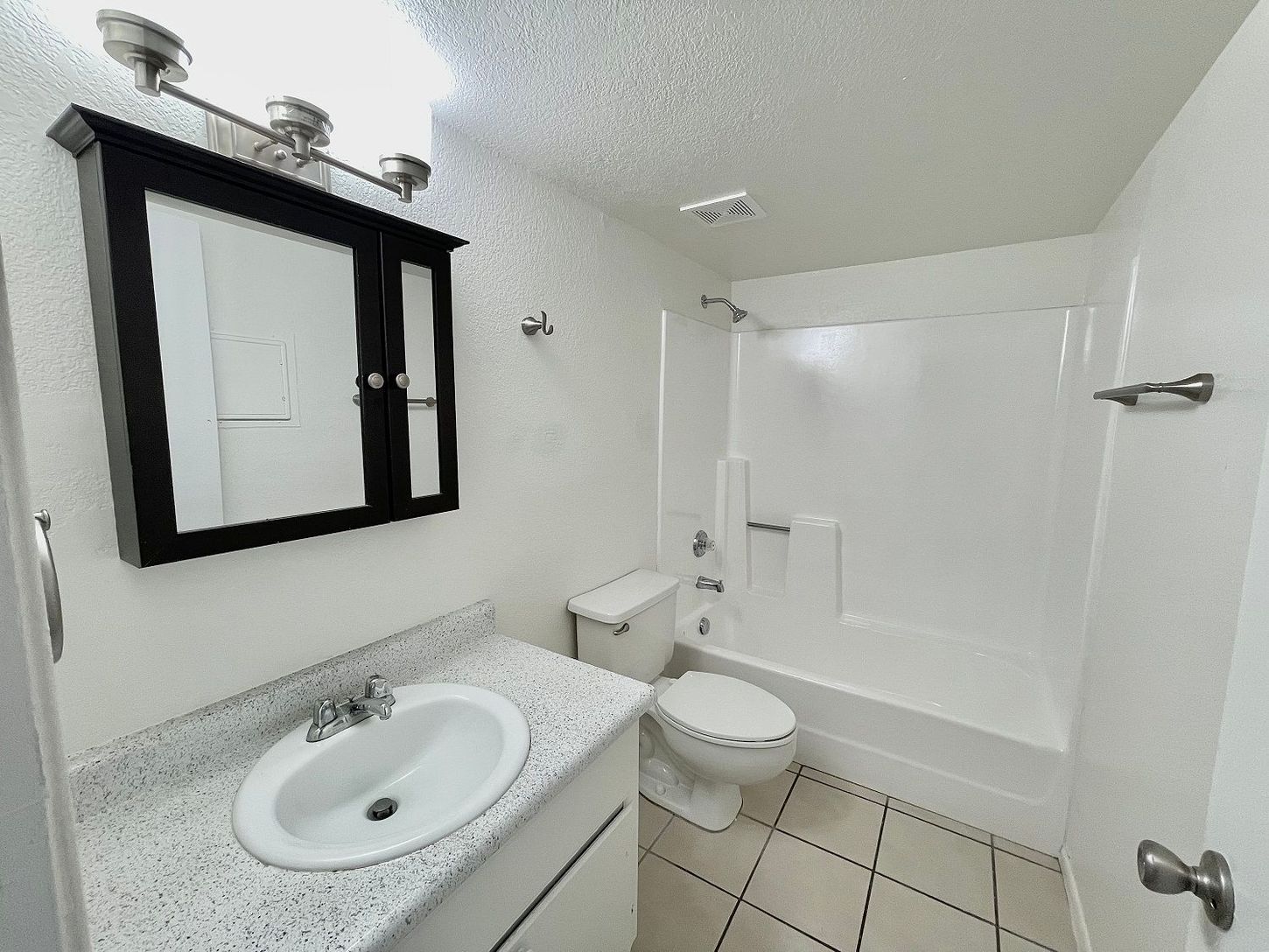 Bathroom with white fixtures, vanity, toilet, shower/tub combo, and black-framed mirror.