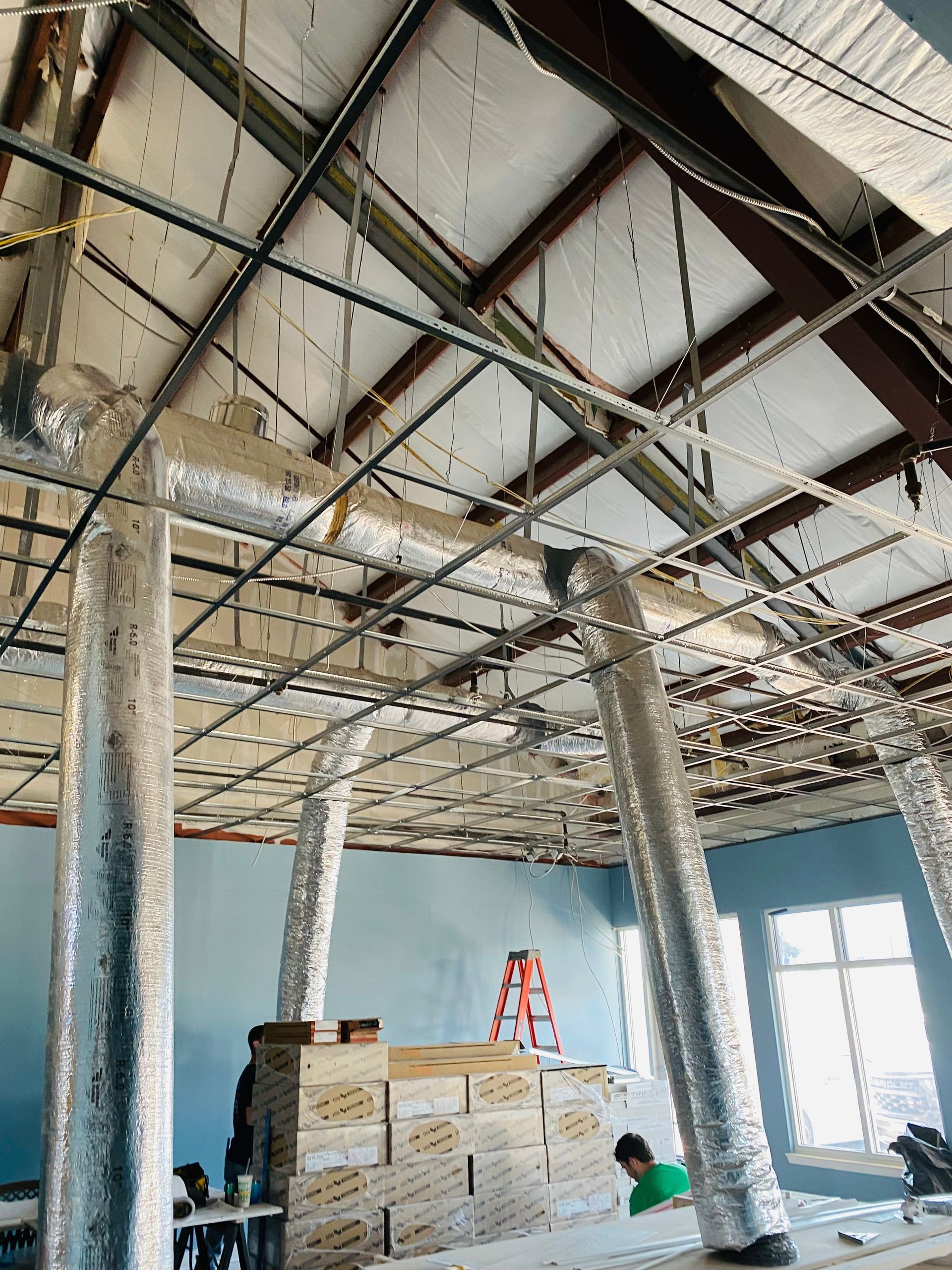Ceiling under construction with exposed beams, hanging wires, and stacked materials in a room
