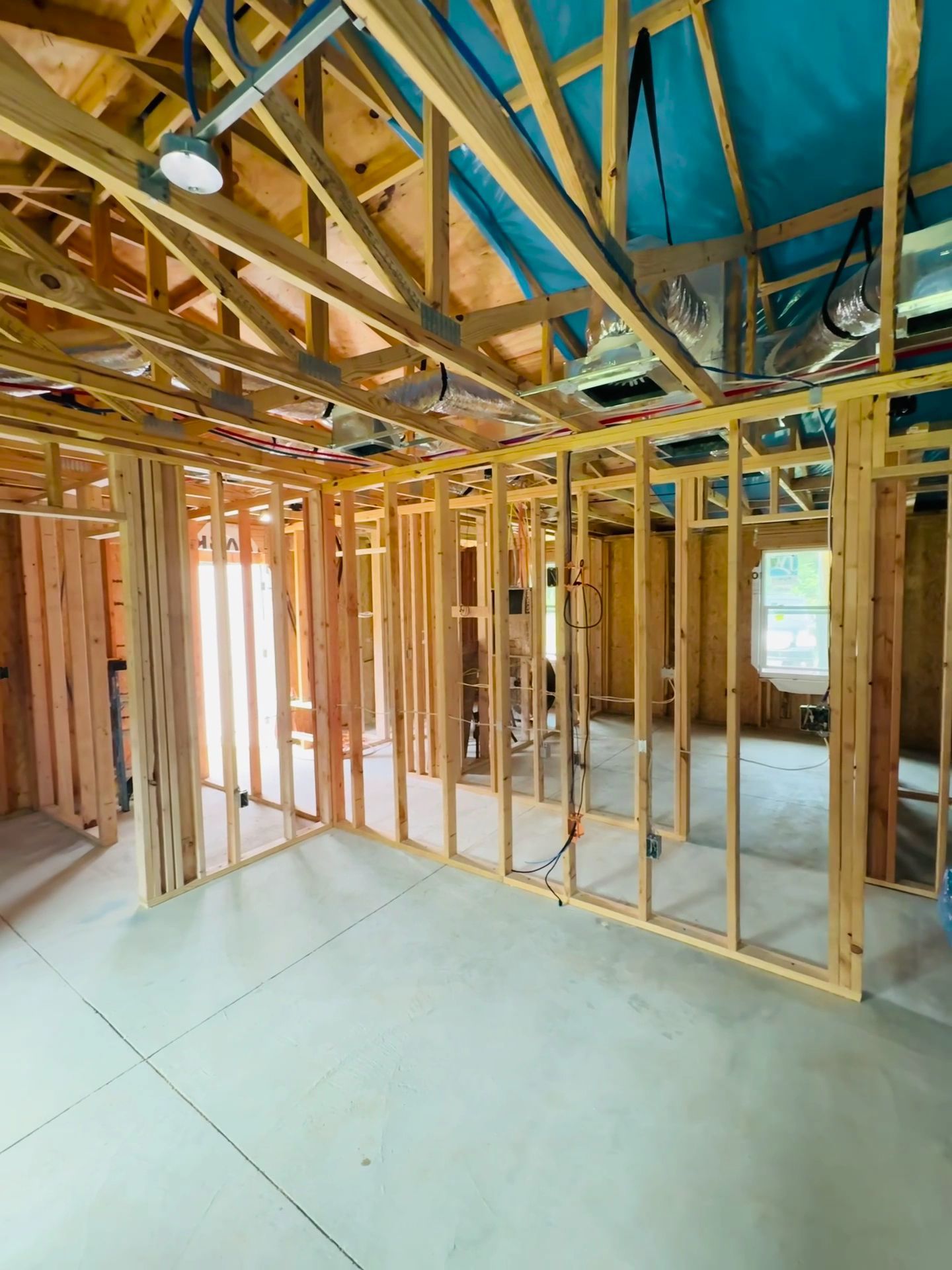 Framed interior of a house under construction with exposed wood studs, beams, and blue roof tarp.