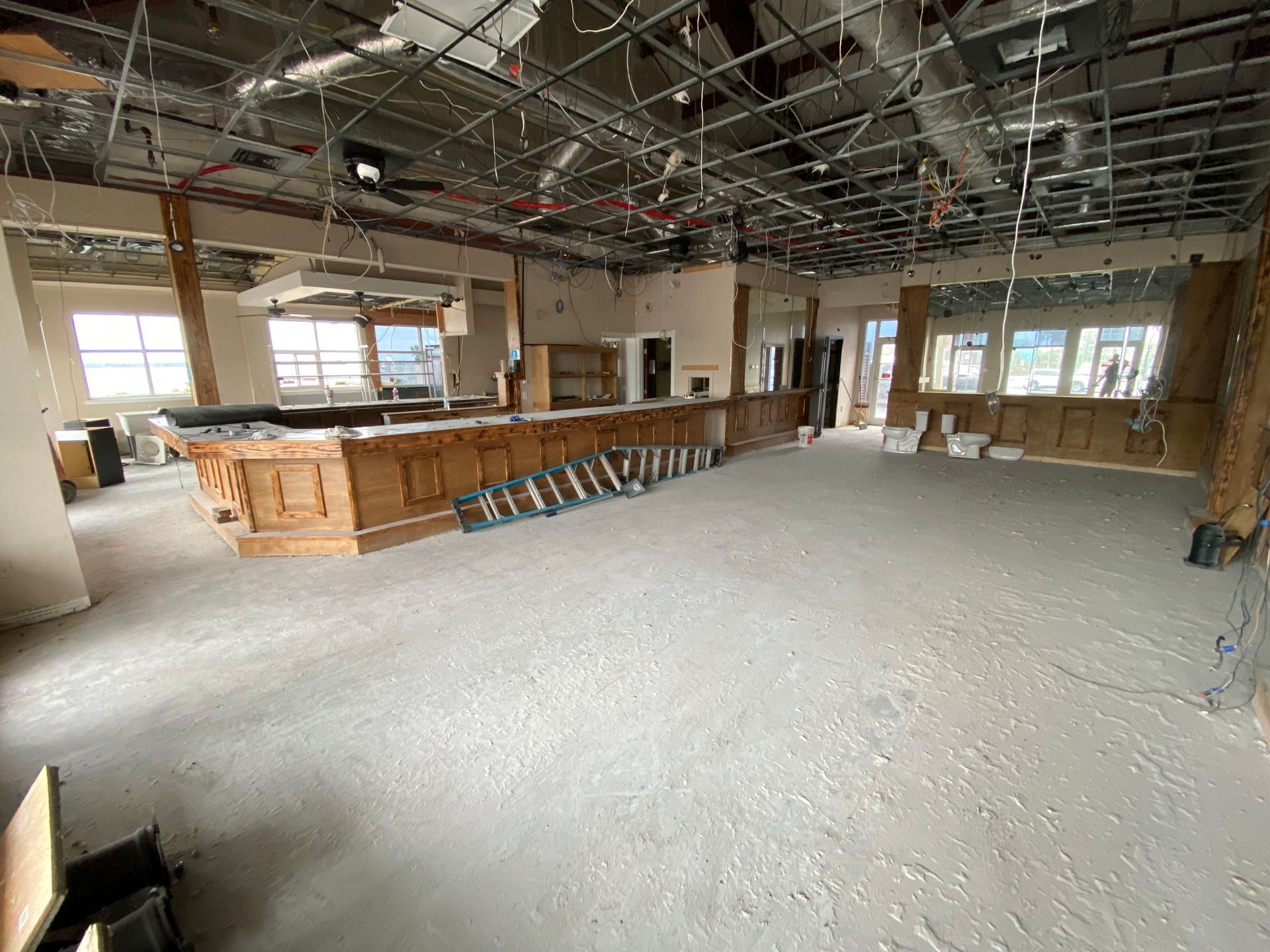 Large unfinished room with exposed ceiling, wood bar counter, and windows along the walls