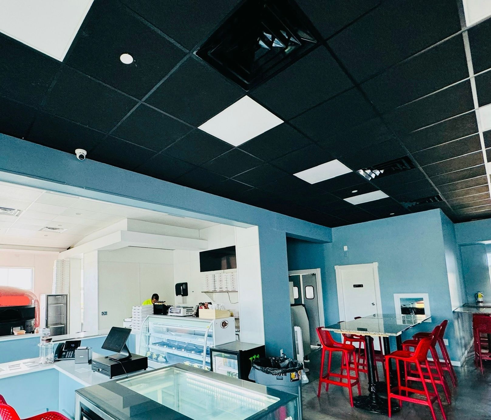 Bright modern café interior with blue walls, black ceiling, white tables, and red chairs