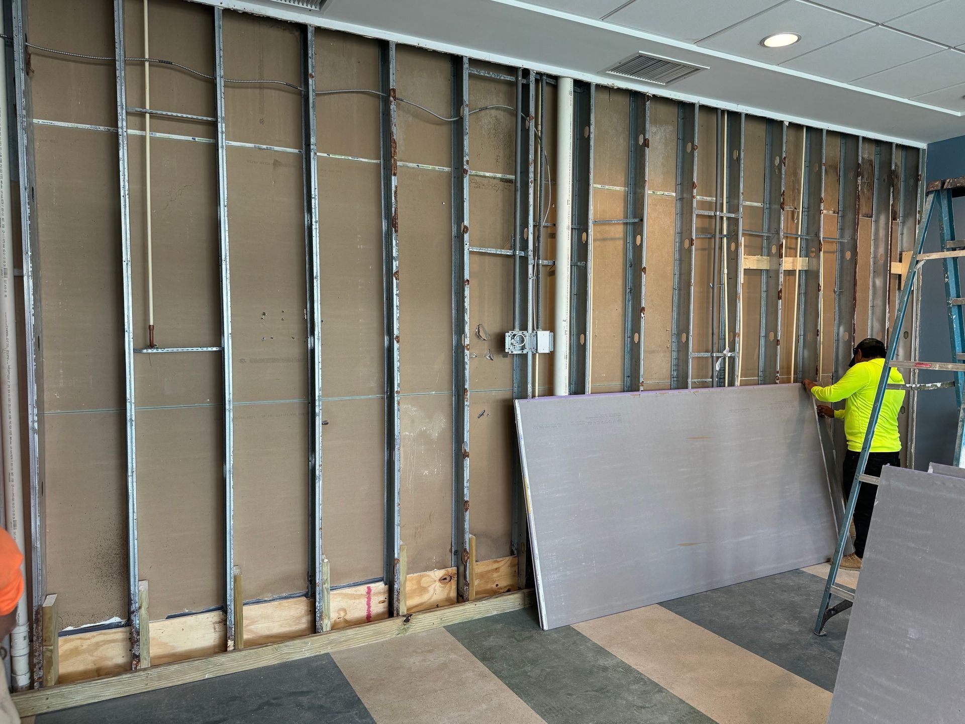 Workers installing wall framing in a room with exposed studs and insulation boards leaning against the wall.