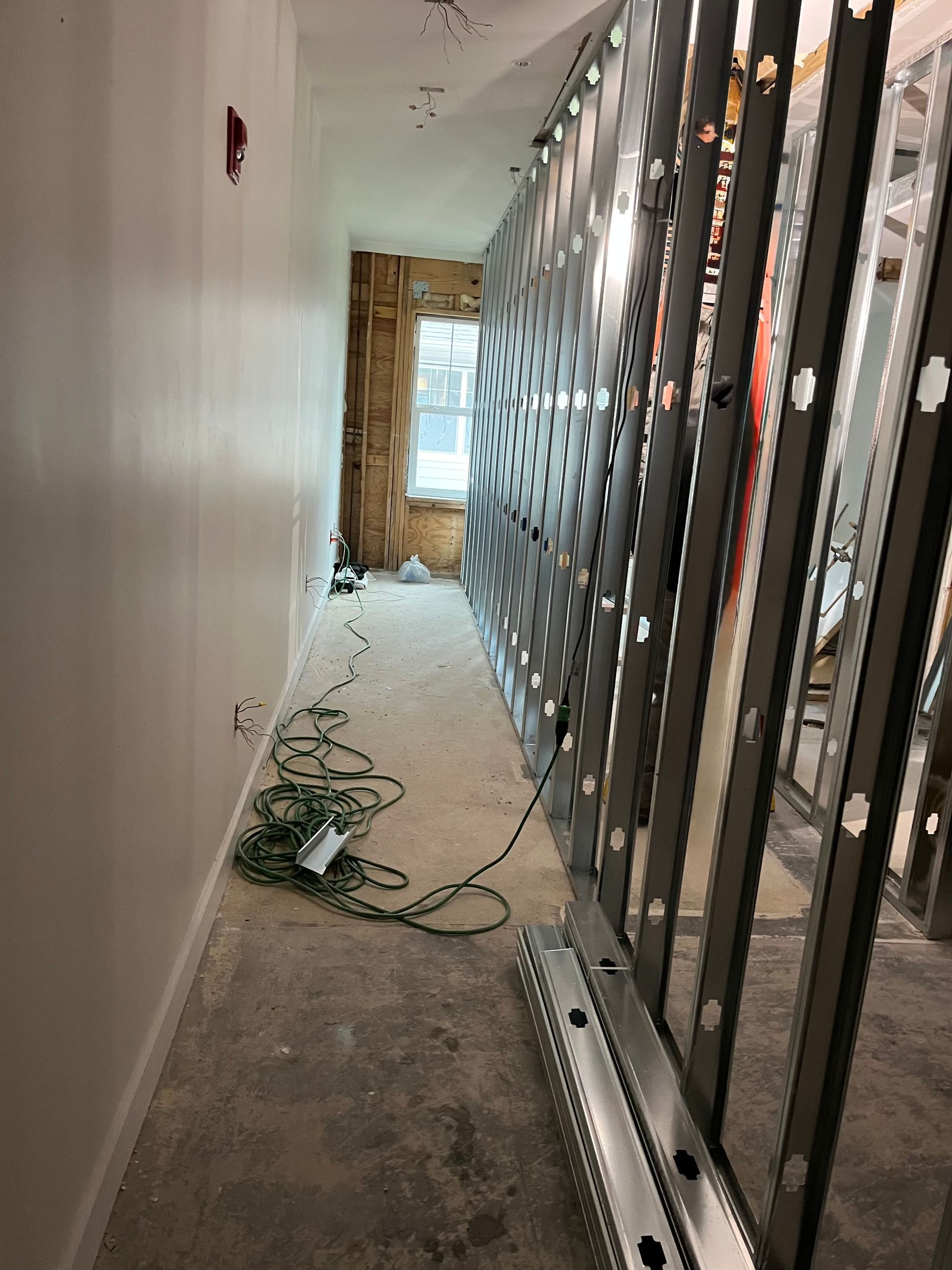 Narrow construction hallway with exposed wall framing, scattered cables, and debris on the floor