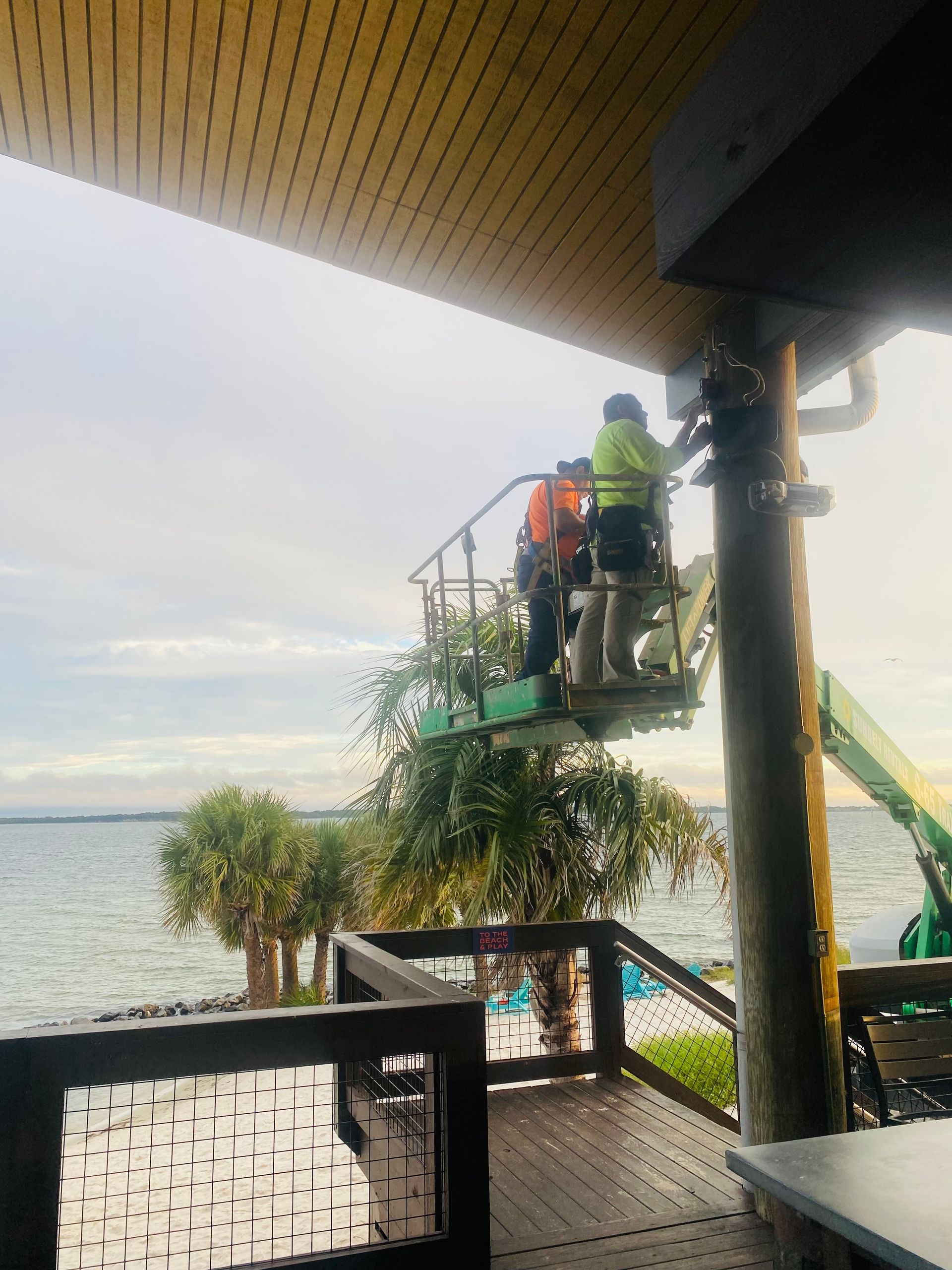 Worker on a lift trimming tree branches beside a lake under a covered deck
