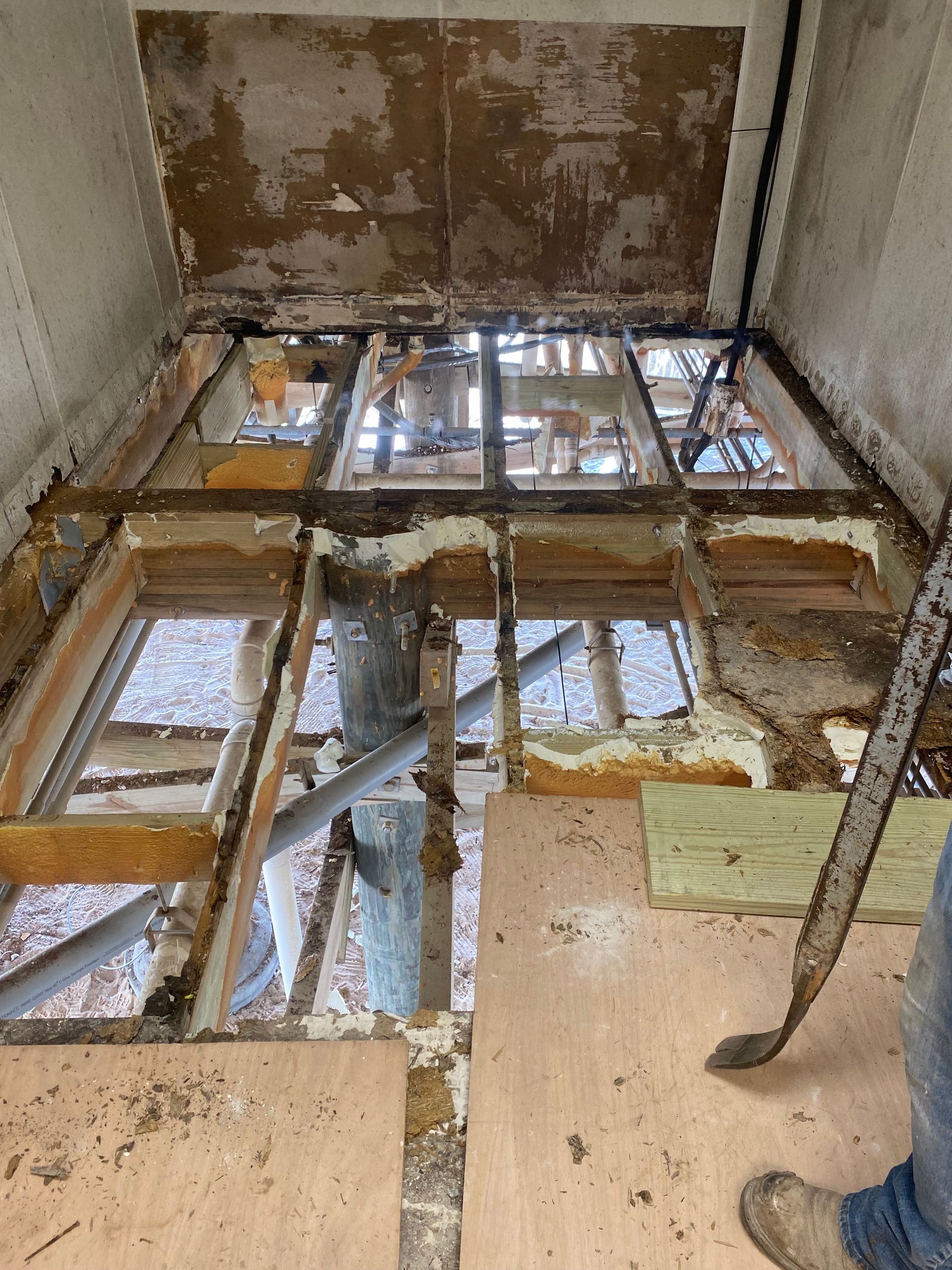 Partially dismantled floor with exposed joists and debris in a damaged room