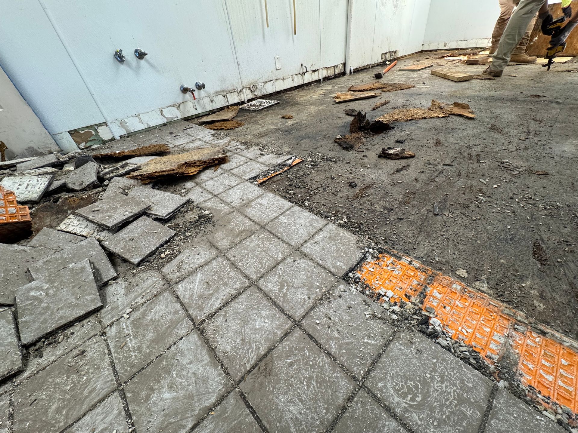 Damaged sidewalk with broken pavers, debris, and orange safety marking beside a wall
