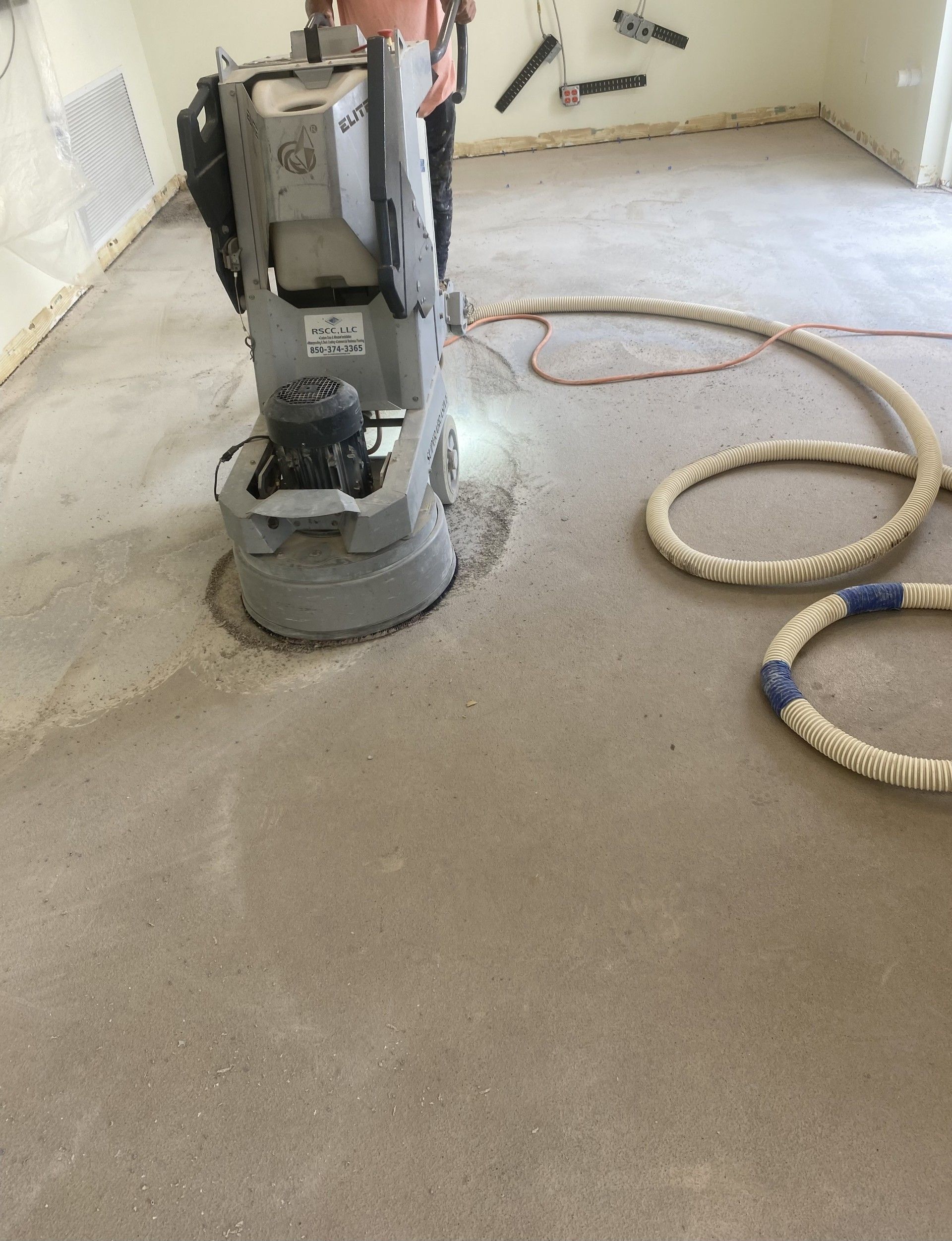 Floor sanding machine on a dusty room floor with coiled hoses nearby.