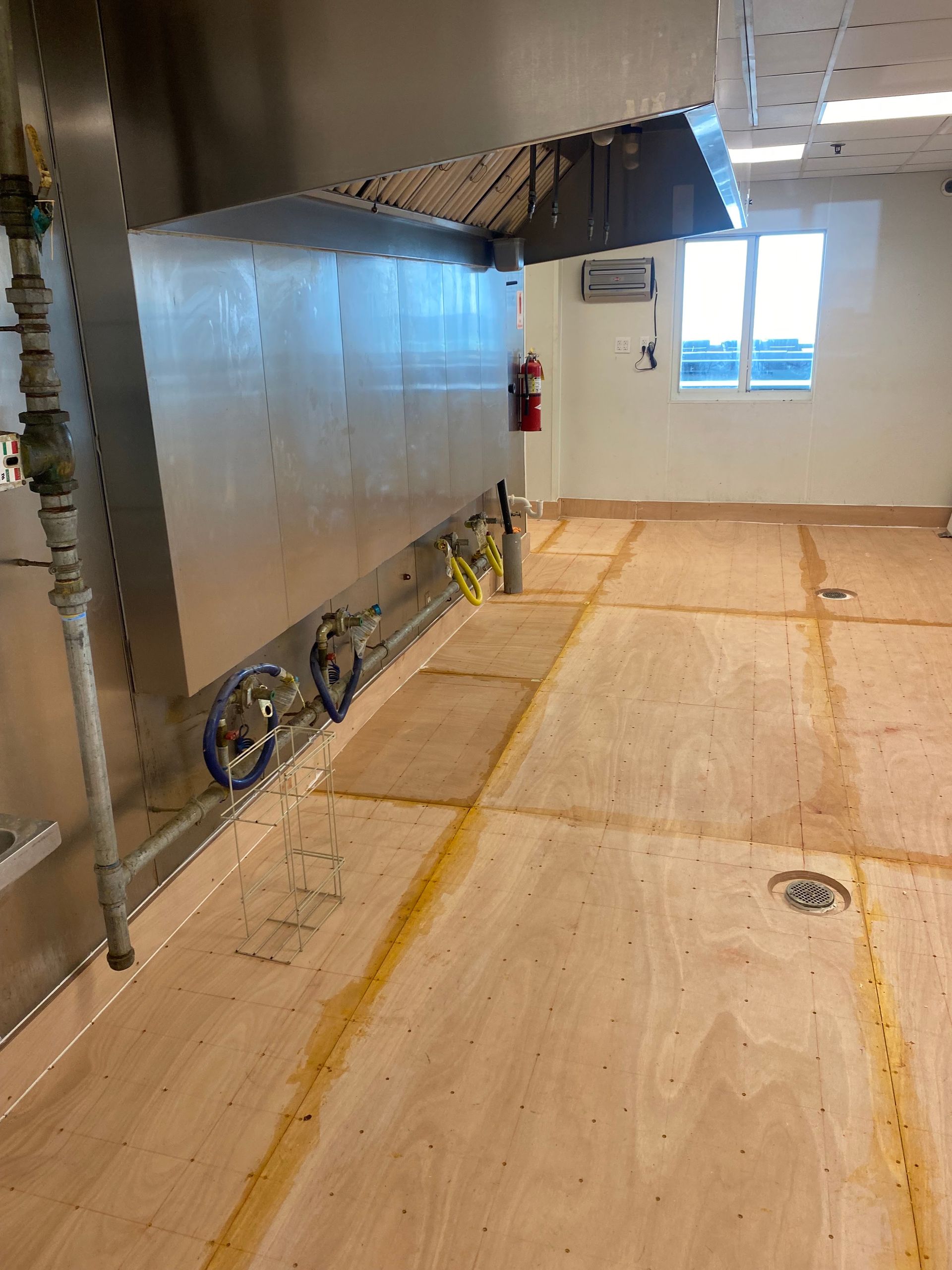 Large room under construction with unfinished floor, metal wall panels, and a window at the back.