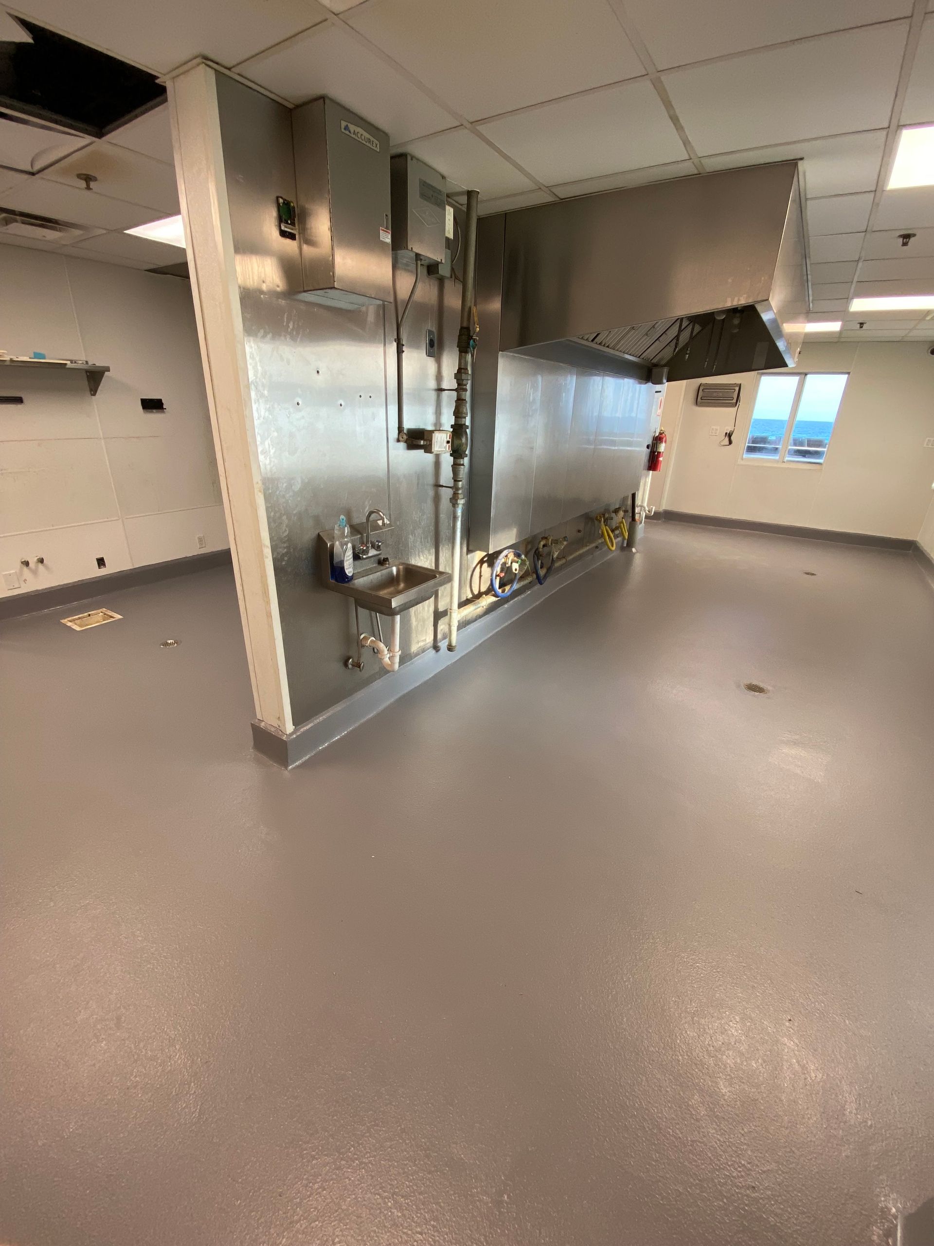 Empty modern commercial kitchen with stainless steel equipment and speckled gray floor