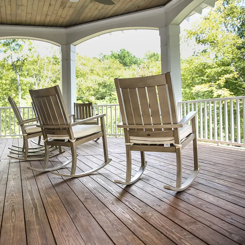 Covered wooden porch with two rocking chairs overlooking a green backyard